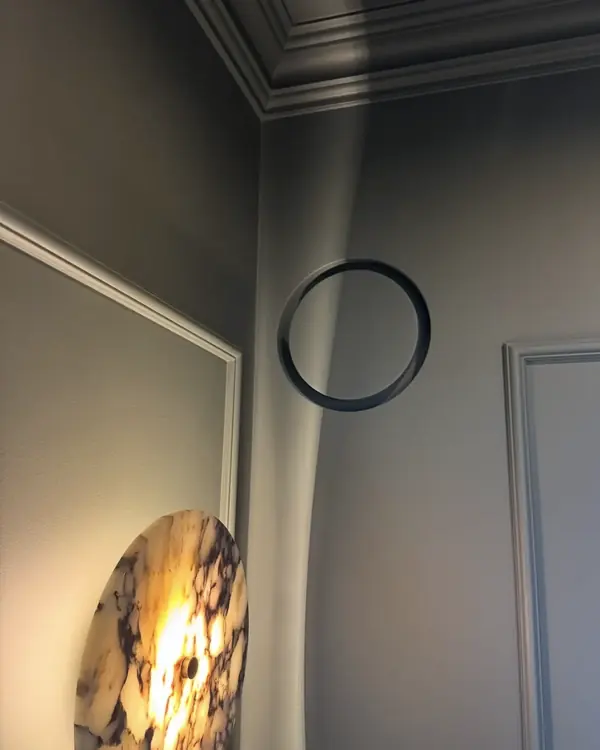 Sztukateria pod sufitem, okrągłe lustro i kamienny kinkiet w grafitowej łazience