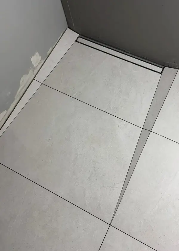 Odpływ liniowy przy ścianie i podłoga z dużych jasnych płyt docinanych w klin pod spadek